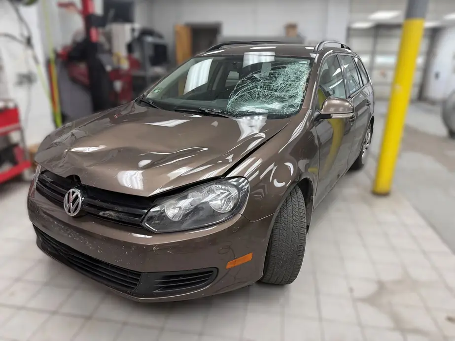Brown Volkswagen Jetta wagon with front-end collision damage and a smashed windshield in the New Central bay